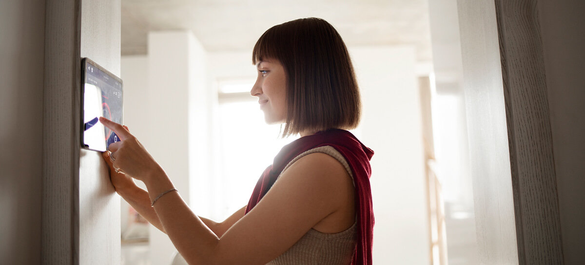 Woman adjusting hvac smart thermostat in a bright room.